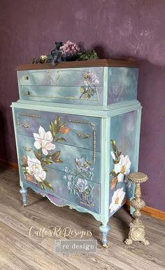 an old dresser painted in blue with flowers on the front and sides, sitting against a purple wall