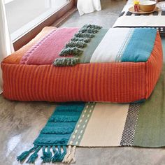 an orange and blue blanket sitting on top of a floor next to a bed in a room