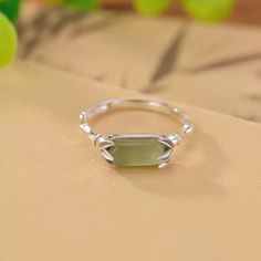 The Serenity Jade Sterling Silver Ring is an exquisite piece, showcasing a 10mm wide and 5mm tall serene jade stone as its centerpiece. Crafted from high-quality S925 sterling silver, this ring offers both elegance and durability. Weighing approximately 2 grams, it features a refined band design with a 2mm thickness, providing a comfortable fit. The ring's inner circumference ranges from 54 to 60mm, accommodating various finger sizes. Due to lighting and display differences, the actual product color may slightly vary, adding to the uniqueness of each piece. This ring embodies sophistication and timeless style. Jade Rings With Natural Stones For Gift, Elegant Green Opal Ring In Sterling Silver, Gift Rings With Natural Jade Stones, Silver Emerald Ring With Rectangular Stone For Gift, Silver Emerald-cut Emerald Ring As Gift, Adjustable Elegant Jade Rings, Jade Open Ring For Gift, Jade Open Ring Gift, Jade Open Ring As Gift