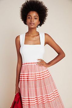 a woman in a red and white dress is holding a handbag while standing with her hands on her hips