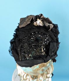 VICTORIAN 19TH C BLACK JET BEAD & LACE BONNET W MOIRE SILK & FLORALS DATING TO THE VICTORIAN 19TH CENTURY THE PICTURES DO NOT DO THIS PIECE JUSTICE FASHIONED OF A LARGE BLACK JET BEAD WIRED ROUND WITH SILK TULLE OVER THE BONING THAT HOLDS IT IN PLACE THE ENTIRE BRIM IS BONED WITH A POINT IN THE FRONT WITH BLACK CHANTILLY LACE FRILLS FULLY AROUND THE BRIM AND IS DENSE ON THE TOP MIDDLE WITH BROWN MOIRE SILK RIBBONS AND MINIATURE FLORALS THE TIES ARE IN BLACK SILK FAILLE CONDITION:  ONE TIE NEEDS Black Victorian Costume Hat With Curved Brim, Victorian High Crown Black Hat, Vintage Fitted Bonnet For Costume, Elegant Adjustable Black Bonnet, Black Victorian Evening Hat, Black Victorian Dress With Lace Trim, Bead Lace, Lace Bonnet, Black Jet