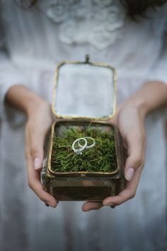 a person holding a box with a wedding ring in it and moss growing inside the lid