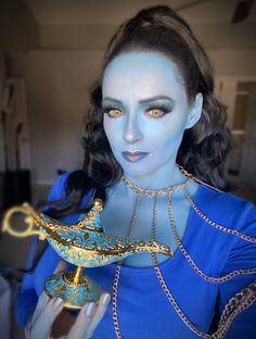 a woman with blue makeup holding a golden teapot