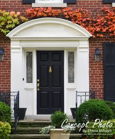 a black front door with white trim surrounded by plants and bushes in front of a brick building