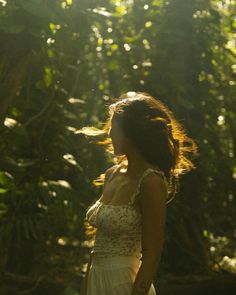 a woman in a white dress is walking through the woods with her hair blowing in the wind