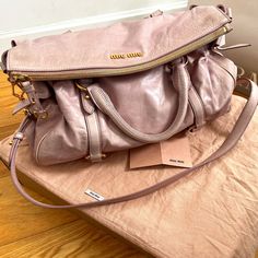 Authentic Miu Miu Vitello Lux Large Bow Bag In Mughetto. A Beautiful And Sophisticated Shade Of Dusky Pink. Minimal Use Has Preserved The Bag In Gently Loved Vintage Condition. Some Light Discoloration On Exterior That Comes From The Natural Aging Of Premium Leather And Hardware As Shown In Photos. Interior Is Pristine. Can Likely Be Serviced At Any Leather Goods Shop To Be Brought To Premium Condition. The Bag Features Rolled Leather Top Handles With An Optional Shoulder Strap, Leather Straps And Brass Links, Decorative Side Leather Bows And A Top Zipper And Zipper Pull. This Opens To A Deep Purple Interior With A Zippered Pocket Branded With Miu Miu Logo Hardware. Approx Measurements: Miu Miu Logo, Purple Interior, Miu Miu Bag, Bow Bag, Natural Aging, Dusky Pink, Large Bow, Leather Bows, Vintage Bags