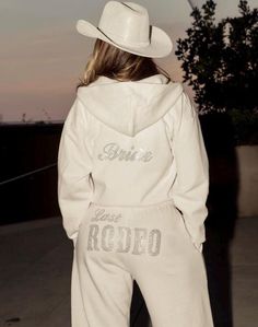 a woman wearing a white hoodie and matching pants is standing on the sidewalk with her back to the camera