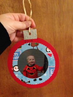 a hand holding a christmas ornament with a baby's photo on it