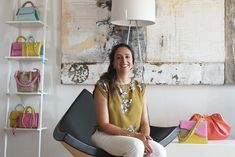 a woman sitting on a chair in front of a wall with handbags and purses