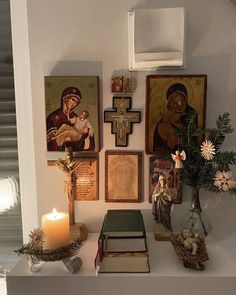 a shelf with pictures and candles on top of it in front of a wall mounted cross