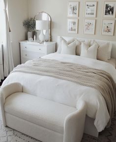 a white bed sitting in a bedroom next to a window with curtains and pictures on the wall