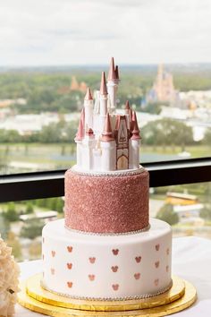 a three tiered cake decorated with pink and white frosting, topped with a castle