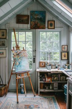 an artist's easel in front of a window with paintings on the wall