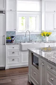 a kitchen with white cabinets and marble counter tops, yellow flowers on the window sill