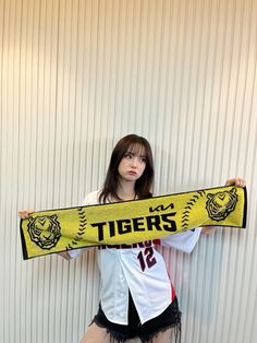 a woman holding a yellow tiger scarf in front of a white wall with the words tigers on it