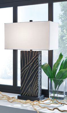 a table lamp sitting on top of a window sill next to a vase with a plant in it