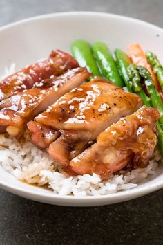 a white bowl filled with rice and meat next to asparagus on a table