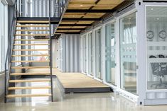 an office building with glass walls and stairs leading up to the second floor that is made out of shipping containers