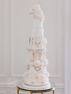 a three tiered wedding cake with white flowers and gold accents on a glass table