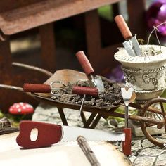 an old wheelbarrow with gardening tools on it and other garden implements in the background