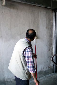 a man holding a red and white baseball bat in his hand while standing next to a building