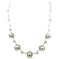 18k white gold necklace with diamond swags or scallops with diamond flower spacers and five graduating gray round cultured pearls draping across the front. The necklace has a plunger clasp with a figure eight safety. The pearls measure approximately 10.5 - 12mm. The approximate total diamond weight is 3.5 carats. Formal Tahitian Pearl Necklace, Gray Round Necklace For Formal Occasions, Elegant Gray Necklace For Wedding, Formal Gray Tahitian Pearl Jewelry, Luxury Gray Jewelry For Formal Occasions, Gray Luxury Jewelry For Formal Occasions, Elegant Gray Round Pearl Necklace, Elegant Gray Pearl Necklace, Elegant Gray Jewelry For Formal Occasions