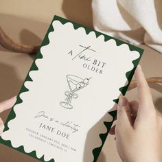 a person holding up a green and white card with an image of a martini on it