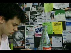 a man looking at his cell phone in front of a wall covered with posters and papers