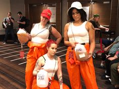 three women dressed in orange and white are posing for the camera while one woman is holding two jugs