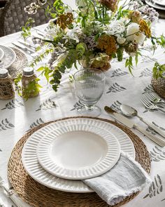 the table is set with plates, silverware and flowers in vases on it