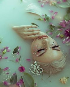 a woman laying in a bath filled with water surrounded by pink and white flower petals