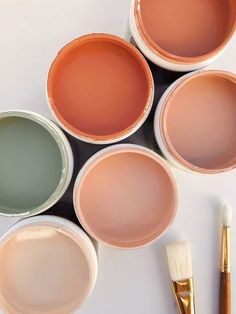 four paint cans with different colors and brushes next to one that has been painted on