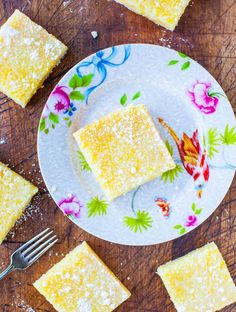 a plate topped with squares of cake next to a knife and fork on top of a wooden table