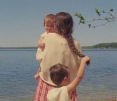 two children are standing on the beach and one is holding onto another child's shoulders