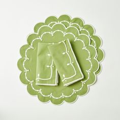 two green napkins sitting on top of a doily with white trim around them