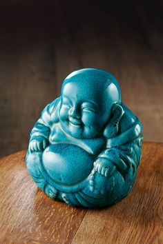 a small blue buddha statue sitting on top of a wooden table next to a cup