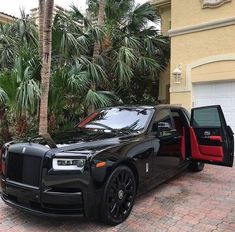 a black rolls royce parked in front of a house with palm trees and a red door