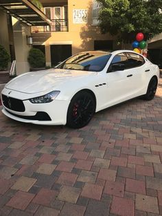 a white masera parked in front of a building with balloons attached to the roof