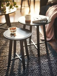 two small tables with cups on them in a living room next to a couch and coffee table