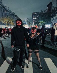 two people wearing masks walking across a crosswalk in the city at night with lights on