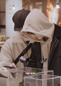 a man in a white hoodie looking at his cell phone while standing next to a clear box