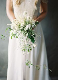 a woman in a white dress holding a bouquet of flowers and greenery on her wedding day