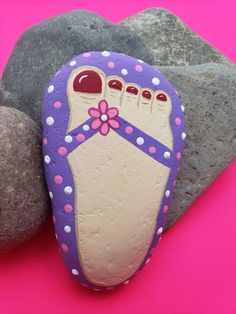 a rock with a foot painted on it sitting next to some rocks and flowers in front of a pink background