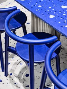 three blue stools sitting next to each other near a table with paint splattered on it