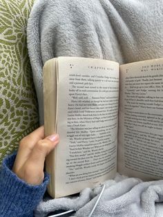 a person is reading a book while laying on a couch with a blanket over their head