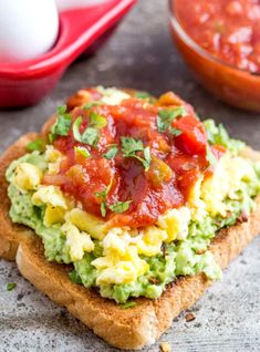 an open face sandwich topped with guacamole and tomato sauce next to eggs