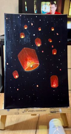 a painting with red lanterns floating in the air on a wooden table next to a bottle