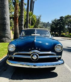 an old classic car parked on the side of the road in front of palm trees