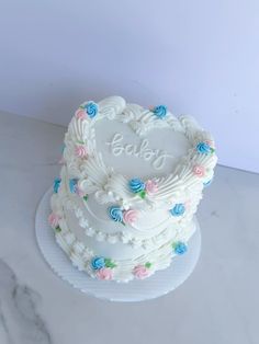 a heart shaped cake with the word baby written on it and flowers around the edges