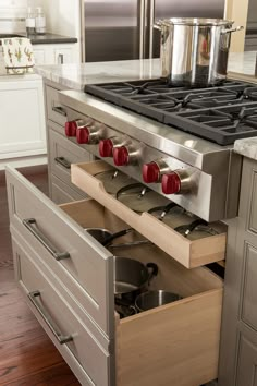 an open drawer in a kitchen with pots and pans on the stove top,